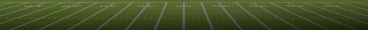A low-angle, wide view of an American football field with white yard lines and markings on green turf.