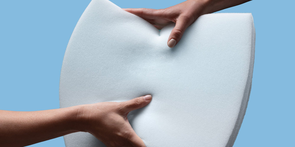 Two hands holding memory foam to demonstrate pressure relief technology with a blue background